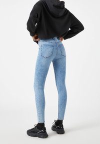 Leggings en jean bleu taille haute avec un léger effet délavé, un design à cinq poches et une coupe ajustée, associés à un sweat à capuche noir et des baskets noires.
