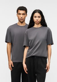 Δύο άτομα φορούν άνετες, γκρι μπλούζες από βαμβακερό μείγμα. Στέκονται δίπλα-δίπλα μπροστά σε ένα ουδέτερο φόντο.