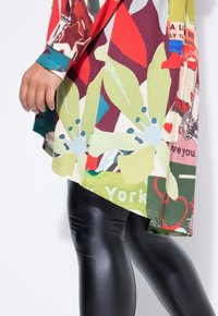 Multikleurige top met gedurfde bloemen- en grafische prints, met een losse pasvorm en lange mouwen; gecombineerd met glanzende zwarte leggings.