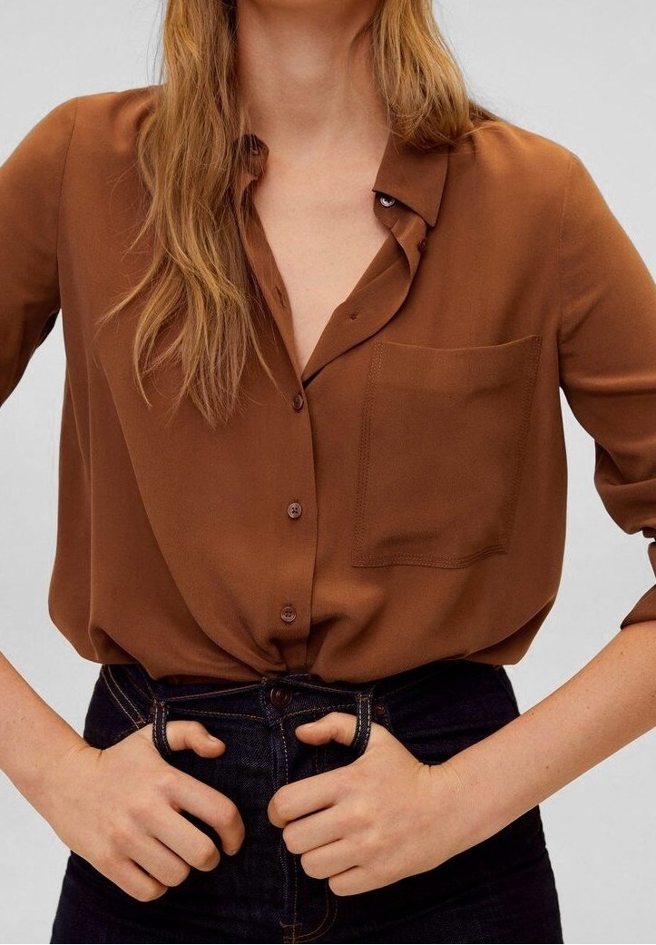 Chemise marron à boutons avec une poche poitrine unique, manches longues et coupe ample. Tissu en mélange de coton avec une texture lisse.