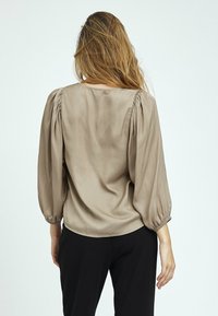 Bluse mit Puffärmeln aus leichtem Taupe-Stoff, mit runder Halslinie und elastischen Bündchen. Glatte Textur mit gerafften Details an den Schultern.