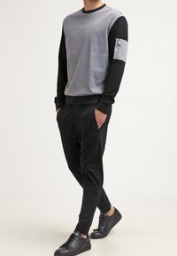Sweat-shirt bicolore gris et noir avec une poche zippée sur la manche, associé à un pantalon noir tapered et des baskets noires.