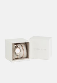 Michael Kors óra ezüst és rózsaarany szíjjal, kerek fehér számlappal, puha belső dobozba zárva, az exterioron logóval.