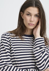 Pikkade varrukatega triibuline tumesinine-kreemjas puuvillane särk; on ümara kaelusega ja lõdvema istuvusega, mansettidel nähtava õmblusega.