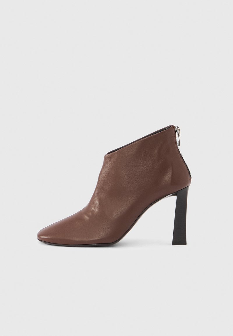 Braune Leder-Stiefeletten mit spitzer Zehenpartie, hohem schwarzen Absatz und hinterem Reißverschluss. Glatte Textur mit schlanker Silhouette.