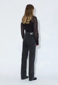 Jeans neri in denim a vita alta con design dritto, dotati di una tasca posteriore e di un'etichetta con marchio sulla cintura. Dettaglio in tessuto texture.