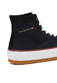 Černé vysoké tenisky vyrobené z plátna aSemiš, s bílými tkaničkami, červeným a černým brandingem, a texturovanou gumovou podrážkou s hnědým okrajem.