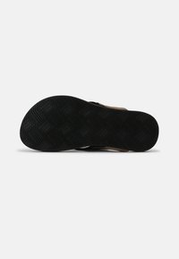 Black rubber outsole with zigzag patterns, featuring a textured surface and a sturdy design. Upper material is brown, likely suede or leather.
