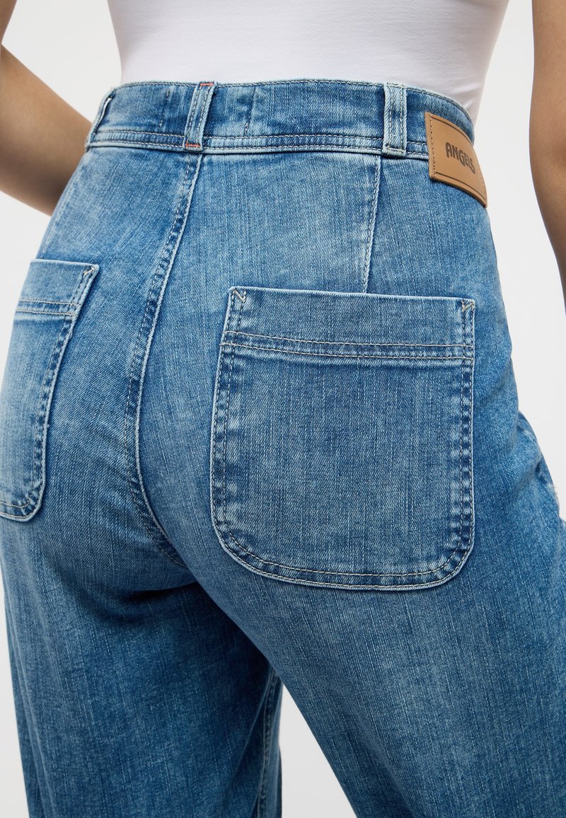 Jeans de mezclilla azul claro con cintura alta, que cuentan con dos bolsillos traseros y una etiqueta de cuero cosida en la parte posterior de la cintura.