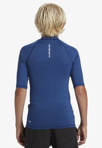 Kortärmad blå rash guard med texturerad tyg, rund halslinning och Quiksilver-logotyp på ryggen, i kombination med svarta shorts.