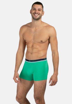 Green boxer shorts made of smooth fabric, featuring a navy waistband with white branding. Cut for a snug fit.