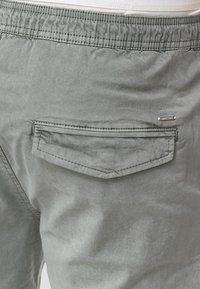 Shorts en coton gris avec une poche arrière à rabat, une taille élastique et un logo métallique en guise d'accent. Texture lisse avec une finition mate.