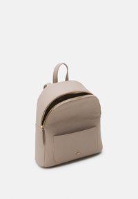 Mochila beige hecha de material texturizado, con un bolsillo frontal, cremallera dorada y correas ajustables. Forma redondeada con diseño minimalista.