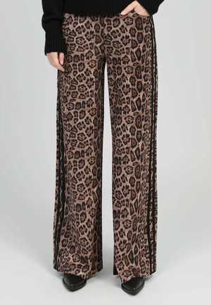 Pantalon à jambes larges avec imprimé léopard marron et noir et bandes latérales, porté avec des chaussures noires et un pull noir.