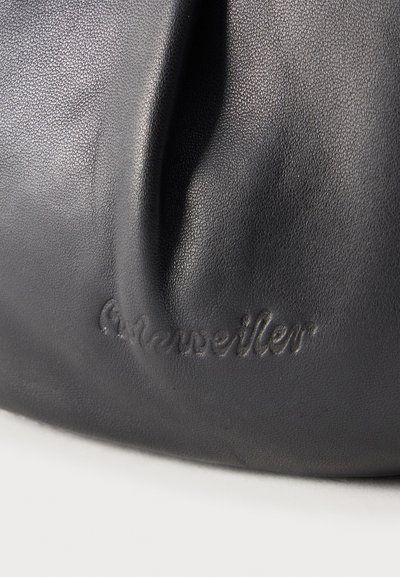 Close-up of black textured leather with embossed "A. Kneissler" logo on a curved surface, showing natural creases and shadows.