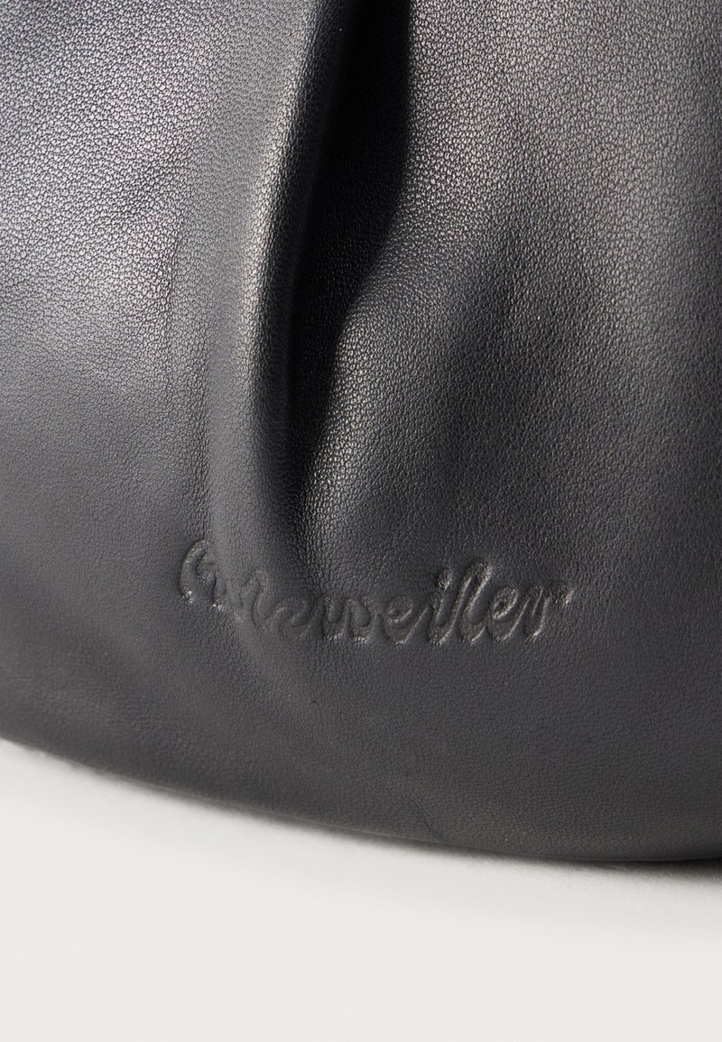 Gros plan sur un cuir noir texturé avec le logo embossé "A. Kneissler" sur une surface courbe, montrant des plis naturels et des ombres.