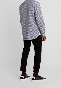 Chemise à carreaux noire et blanche, pantalon slim noir, chaussettes bordeaux et baskets noires avec accents blancs.