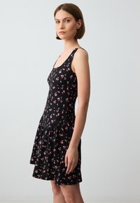 Zwarte bloemenjurk met een nauwsluitend lijfje en dunne bandjes, en een uitlopende rok versierd met kleine roze bloemen. Zachte stoffen textuur.