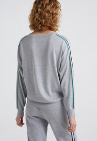 Sweatshirt gris clair à manches longues, avec des poignets et une taille côtelés. Présente des rayures colorées en turquoise, rose et marine le long des manches.