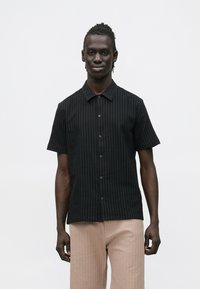 Zwart shirt met korte mouwen, verticale strepen, knoopsluiting aan de voorkant en een kraag. Lichtgewicht stof met een subtiele textuur. Gecombineerd met beige broek.