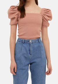 Light pink ribbed top with puff sleeves and a square neckline, paired with high-waisted blue denim jeans.