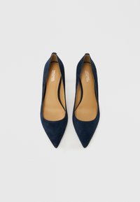 Temno modri semišasti čevlji z visokimi petami, zašiljenim prstom in nizkim izrezom, z bež vložkom. Brez vidne kovinske opreme ali okrasnih elementov.