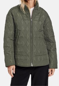 Giacca verde trapuntata con motivo a diamante, colletto alto e chiusura con zip. Realizzata in un materiale sintetico morbido, ha una vestibilità comoda.