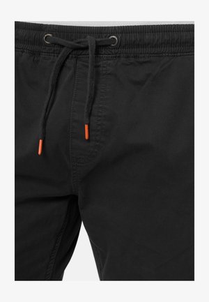 Black shorts with an elastic waistband, featuring a drawstring with orange tips, made from a smooth fabric. Includes side seams for structure.