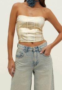 Gouden strapless top van metaal met gestructureerde naden, in combinatie met lichtblauwe high-waisted wijde jeans. Gladde textuur en modern ontwerp.