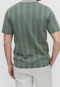 Grön kortärmad polo med en strukturerad randdesign, som har krage och en figursydd passform. Slät tyg.