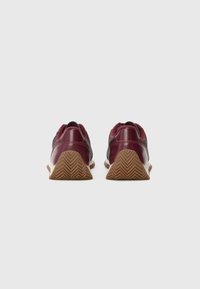 Para burgundowych i brązowych sneakersów pokazanych z tyłu, z gumowymi podeszwami w wzór chevron na gładkim białym tle.