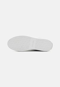 Semelle de sneaker en caoutchouc blanc avec motif circulaire et marque. Texture lisse, design minimaliste et talon arrondi pour la stabilité.