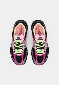 Sapatilhas Nike com parte superior em malha preta, detalhes em rosa e apontamentos prateados refletivos. Atacadores verdes brilhantes e forro interior rosa.