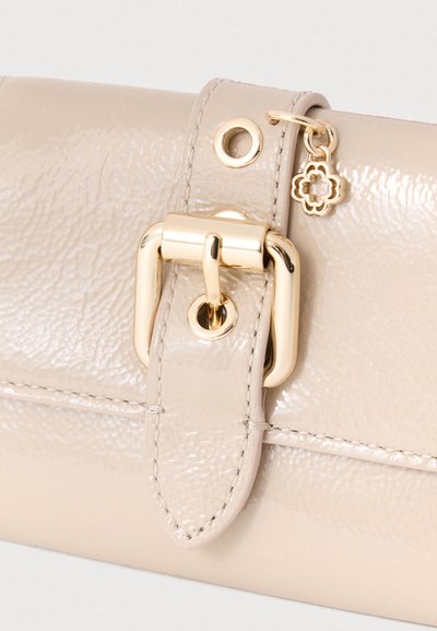 Τσάντα χειρός από μπεζ δέρμα με γυαλιστερή υφή, με χρυσαφί μεταλλική αγκράφα και διακοσμητικά, καθώς και ένα μικρό διακοσμητικό κρεμαστό.