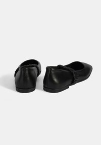 Schwarze Leder-Ballerinas mit einer abgerundeten Zehenpartie und einem elastischen Rüschendetail auf der Rückseite. Flacher Absatz, glatte Textur und einfaches Design.