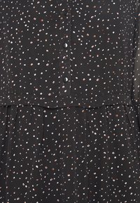 Musta mekko nappikiinnityksellä, jossa on sattumanvarainen kuvio valkoisista ja ruosteen värisistä pisteistä, sekä pitsinen, liehuva hame.