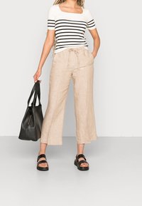 Pruhované černobílé tričko s krátkým rukávem, béžové lněné kalhoty s širokými nohavicemi, černá kožená taška a černé platformové sandály.