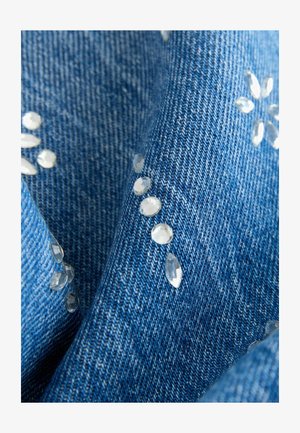 Jeans tkanina v modri barvi z jasno, kot dragi kamen podobno okrasje, razporejeno v obliki cvetov po celotni površini, z vidno teksturo tkanja.