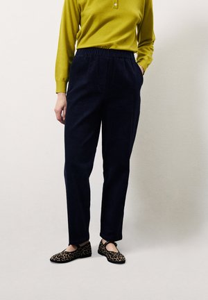Donkerblauwe corduroy broek met een elastische tailleband, gecombineerd met een felgroen langemouwen shirt en zwarte flats met luipaardprint.
