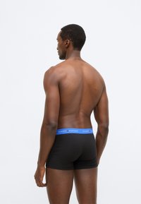 Mustad bokseripüksid sinise vöökohaga, kus on "TOMMY HILFIGER" logo. Kangas näib olevat sile ja disain lihakohane.