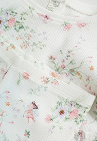 Prenda de algodón con una textura acanalada blanca, que presenta un patrón floral en rosa, morado y verde, con pequeñas figuras ilustradas entre las flores.