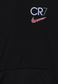Tela negra con texto blanco "CR7" encima del logotipo de Nike en píxeles rojos y blancos, ubicado cerca de la zona del pecho superior.