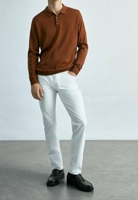 Brown long-sleeve polo, white slim-fit trousers, and black shoes. The polo features a collar and three-button placket. Smooth textures.