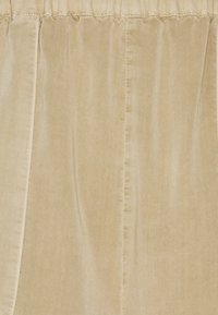 Tessuto in velluto beige con una texture liscia, caratterizzato da pieghe e una fascia elastica in vita. Design morbido e cadente, adatto per un abbigliamento casual.