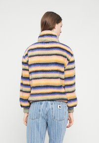 Fleecepullover med høj krave i livlige striber af gul, lilla, blå og sort. Har en afslappet pasform og ribkanten manchetter.