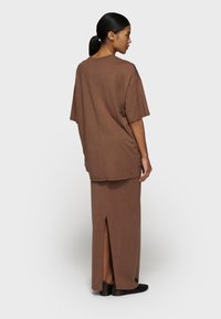 Brun oversized T-shirt med korte ærmer, parret med en matchende nederdel med en slids bagpå. Glat stoftekstur, afslappet pasform, minimalistisk design.