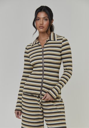 Gestreiftes Zip-up-Oberteil aus geripptem Stoff in Braun, Gelb und Weiß. Mit Kragen und langen Ärmeln, kombiniert mit passenden Hosen.