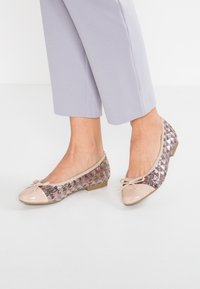 Bailarinas con una puntera nude brillante, parte superior de lentejuelas con patrón en tonos morados y rosas, y un lazo decorativo en el empeine. Suela plana.