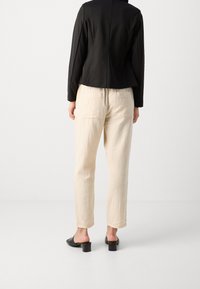 Schwarze taillierte Blazer, cremefarbene strukturierte Hose und schwarze offene Mules mit Blockabsatz, von hinten betrachtet.