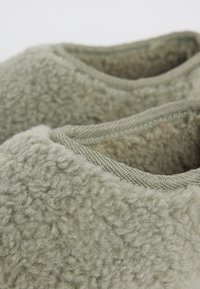 Close-up of light gray fleece fabric with visible soft texture and wool-like fibers around the collar edges of a garment.